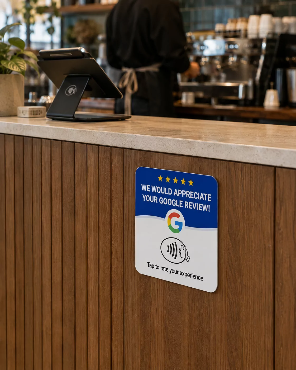 The blue and white review plate on the wood panelling of a cafe counter, with a card terminal and an espresso machine behind it